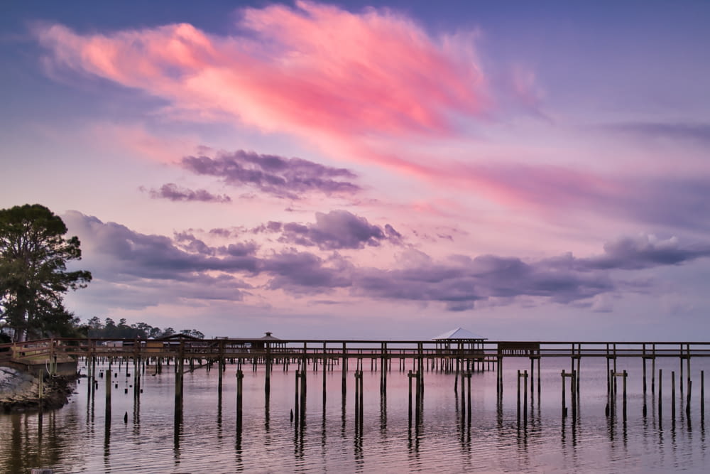 a pink cloud hangs over a pier in the water