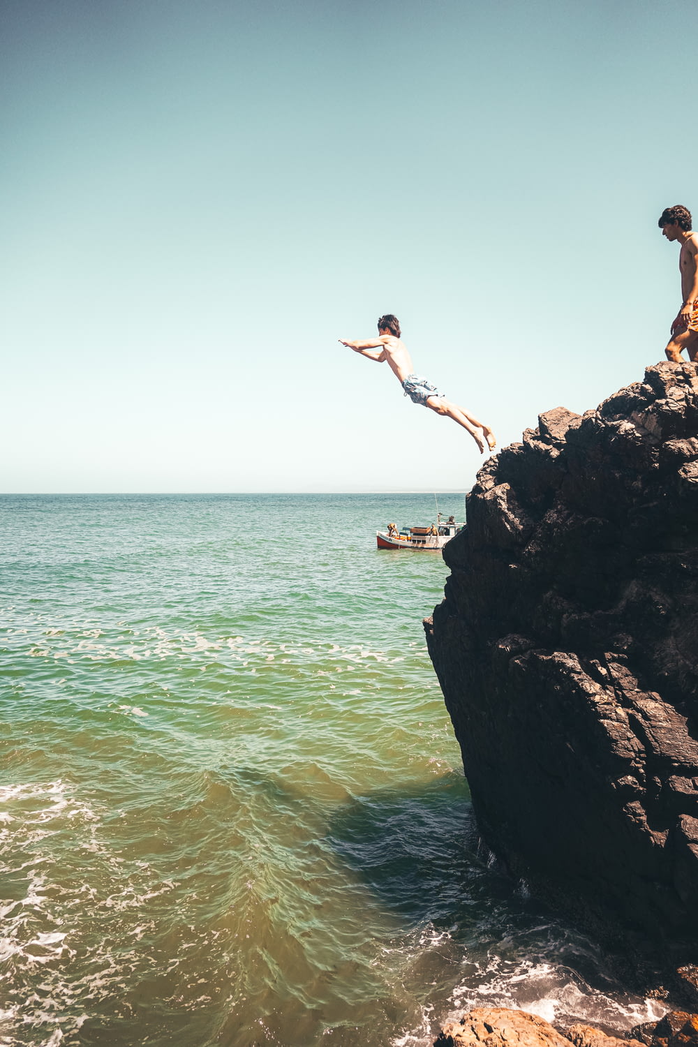 two people jumping off a cliff into the ocean