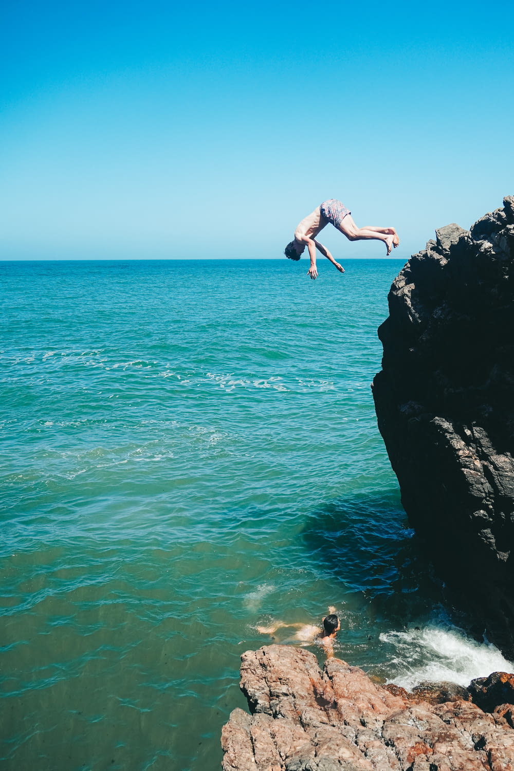 a person jumping off a cliff into the ocean