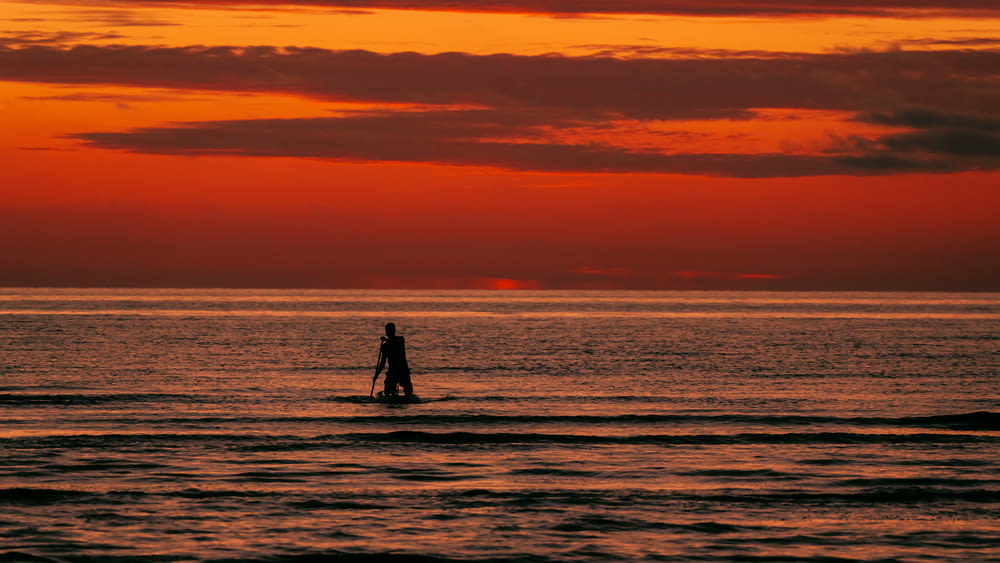 a person standing on a surfboard in the ocean at sunset