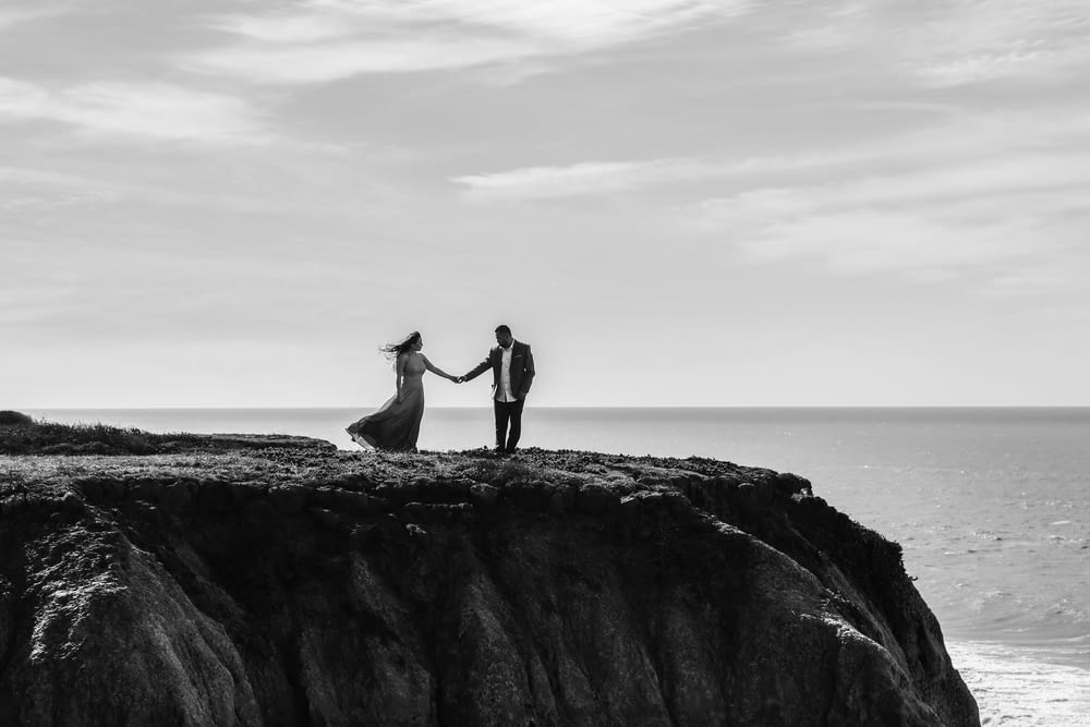 a man and a woman holding hands on top of a cliff