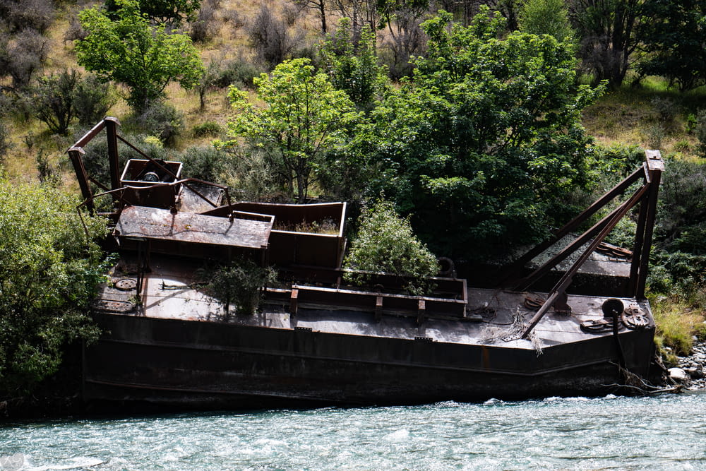 um velho barco enferrujado sentado ao lado de um rio