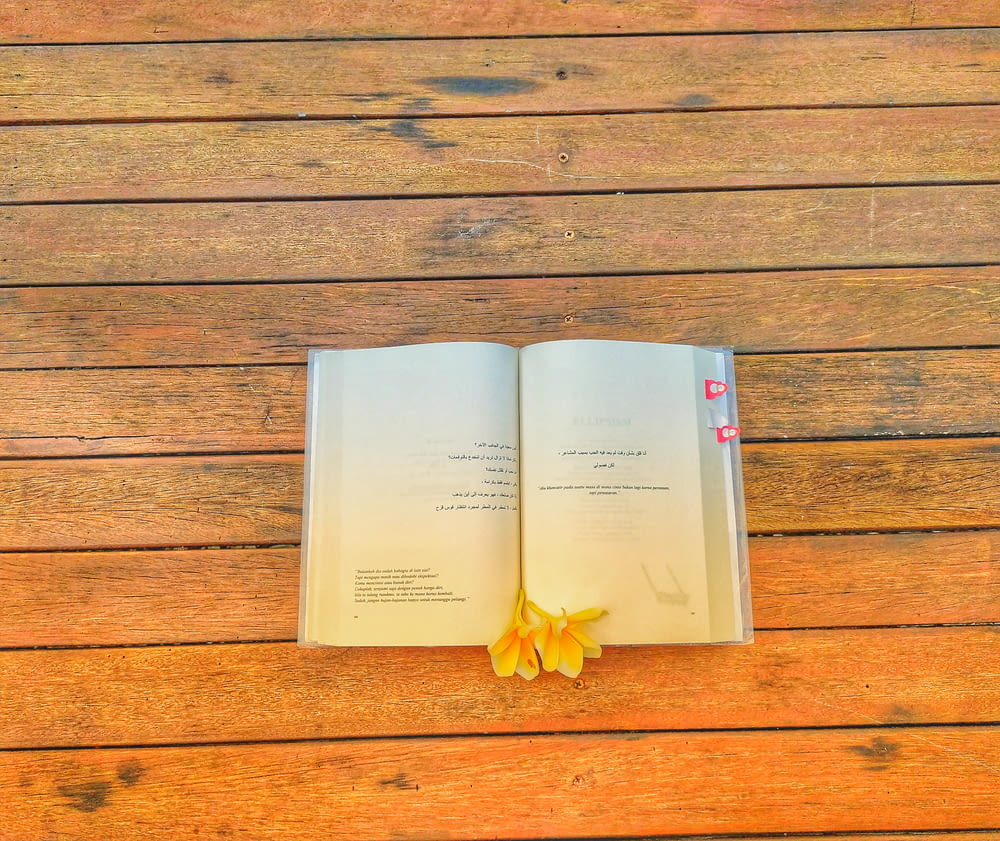 an open book on a wooden table with a flower