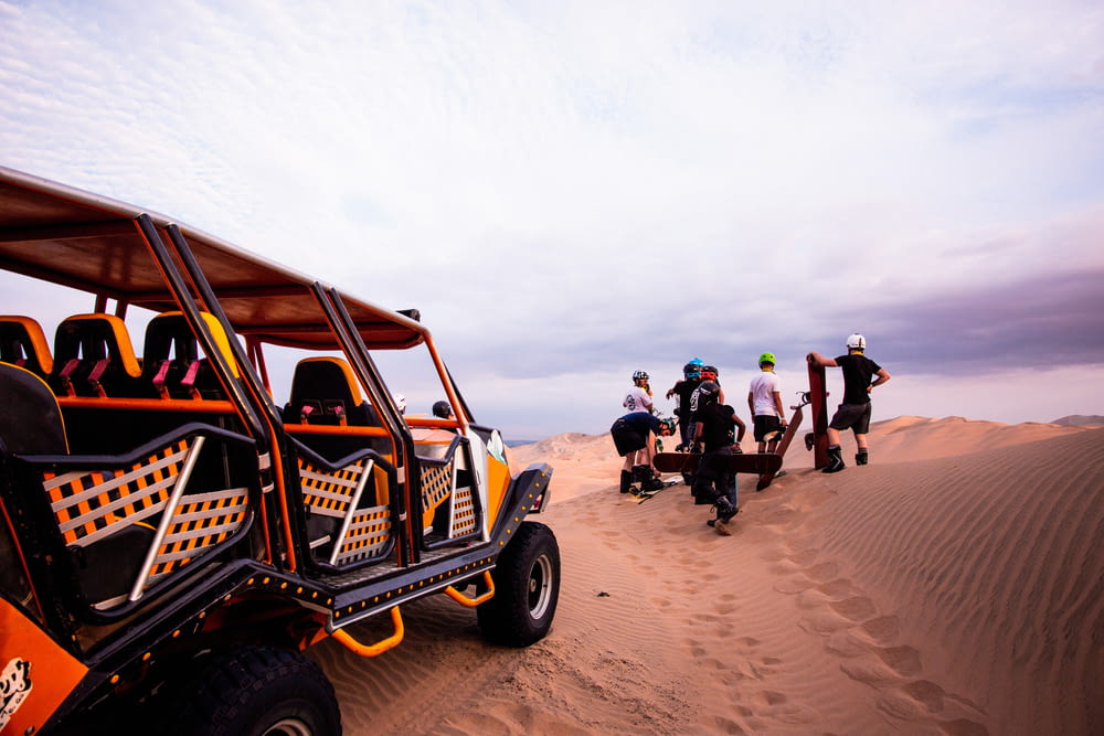 a group of people standing around a buggy in the sand