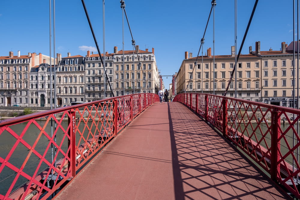 a red pedestrian bridge over a river with buildings in the background