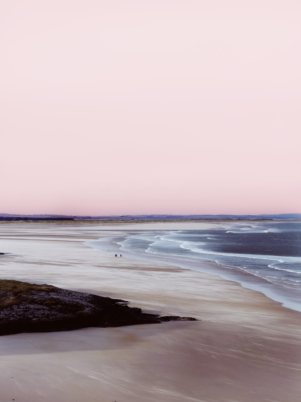 a pink sky over a sandy beach with waves