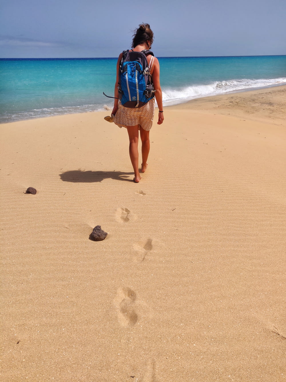 a woman walking on the beach with a backpack