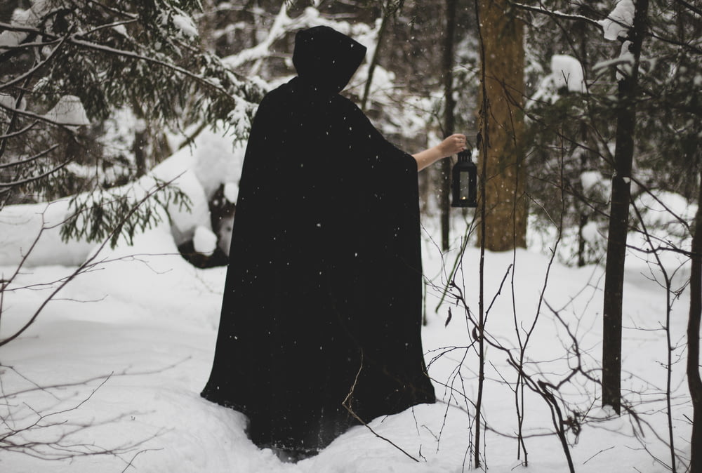 a person in a black cloak standing in the snow