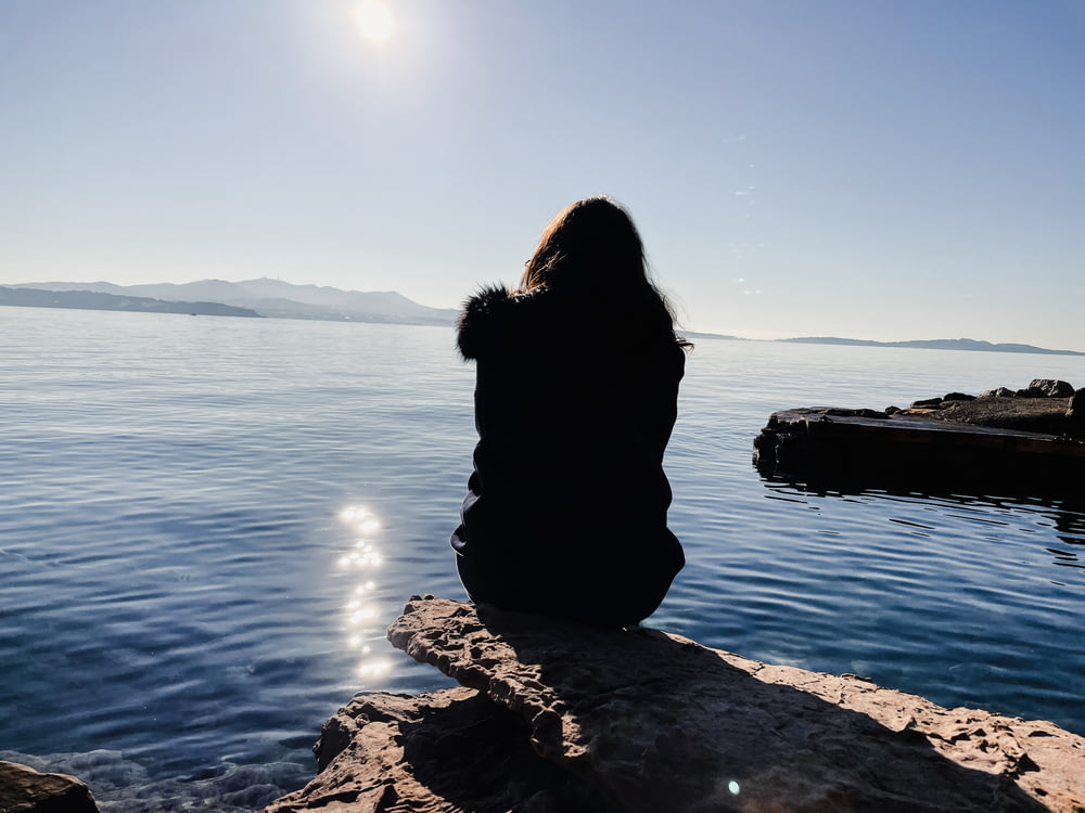 a person sitting on a rock looking out at the water