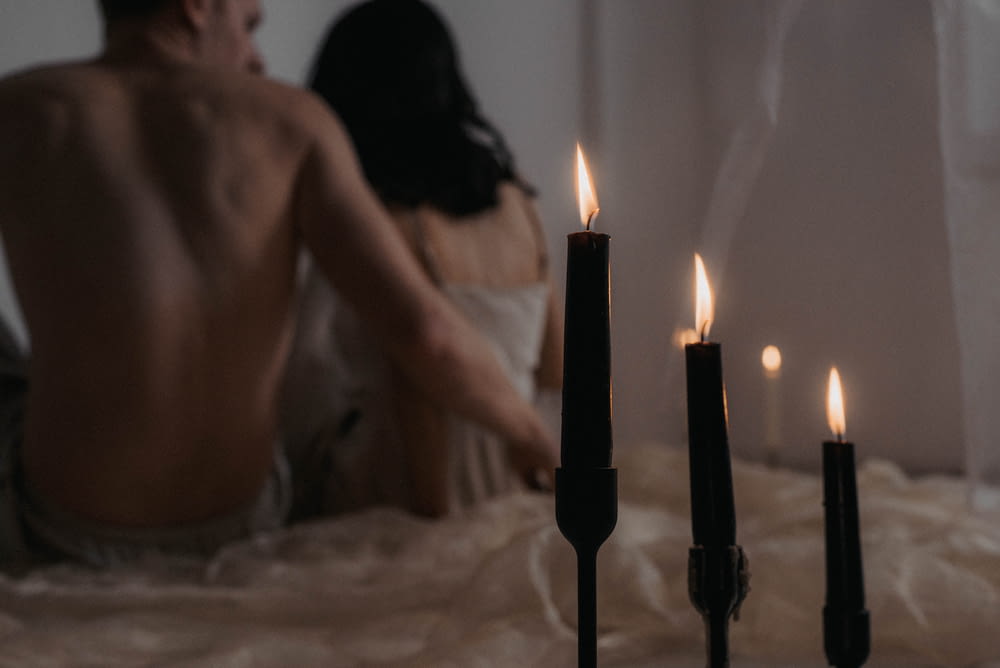 a man and woman sitting on a bed next to candles