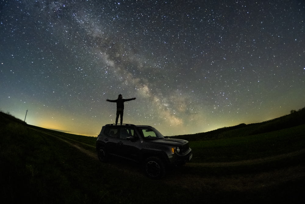 a man standing on top of a car under the stars