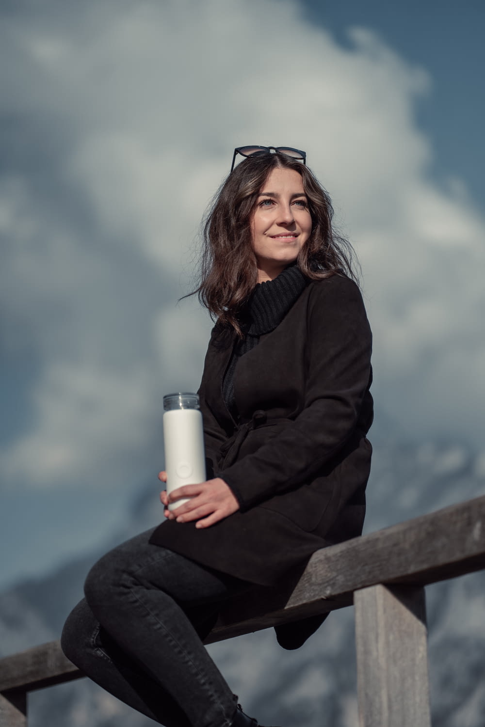 a woman sitting on a rail holding a coffee cup