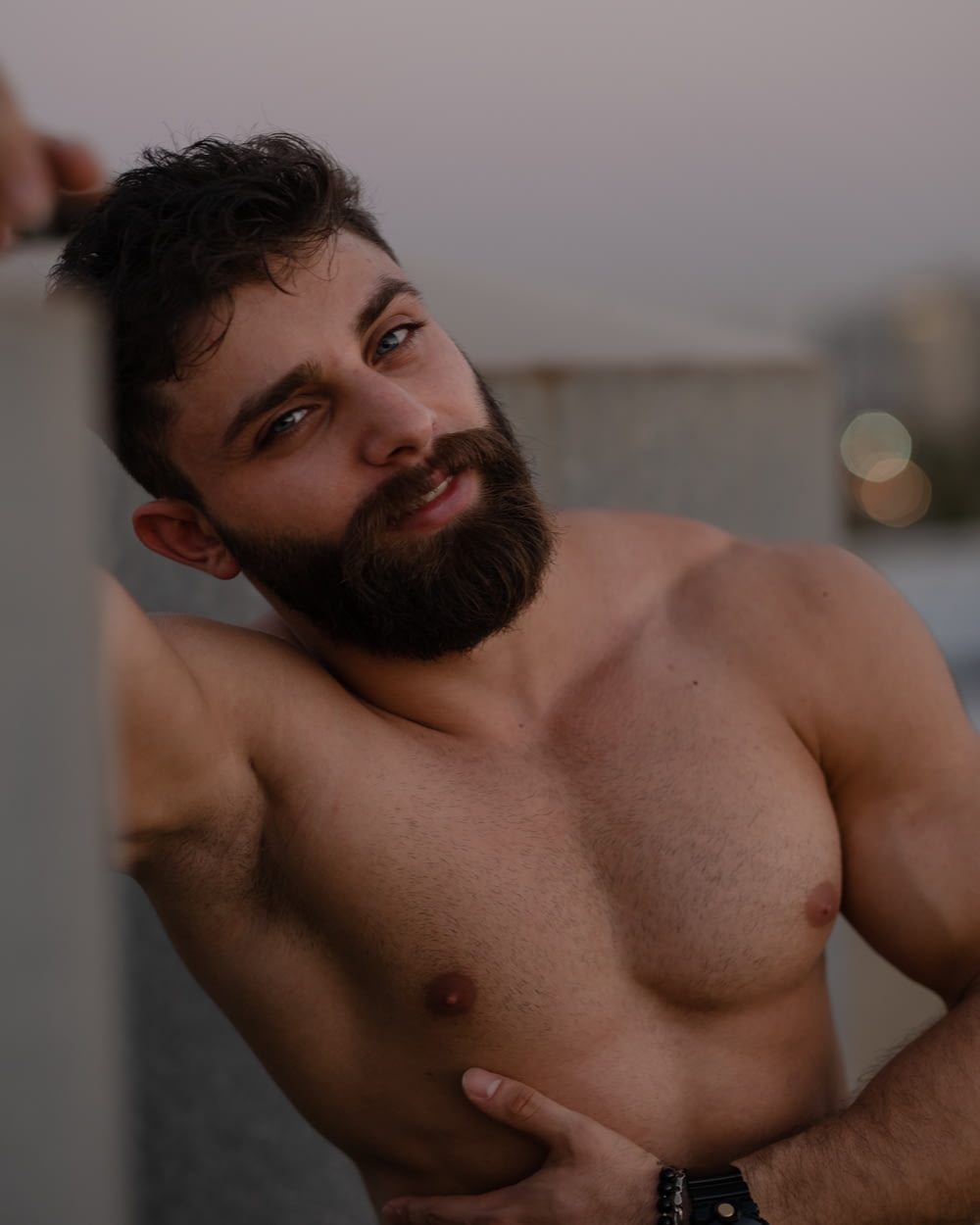 a shirtless man with a beard leaning against a wall