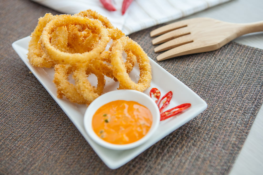 a white plate topped with onion rings next to a bowl of dipping sauce