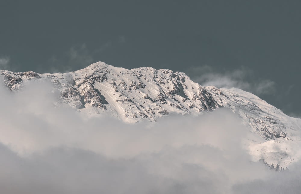 a mountain covered in snow and clouds under a gray sky