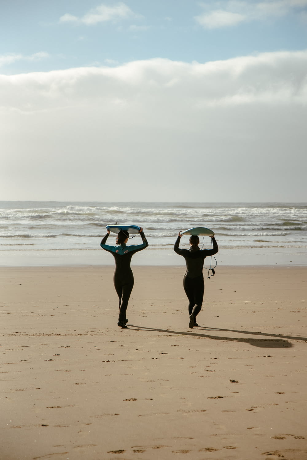 two people walking on a beach carrying surfboards