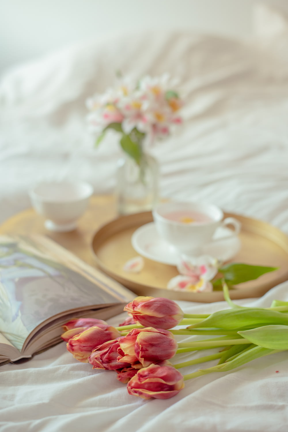 a tray with flowers and a book on a bed
