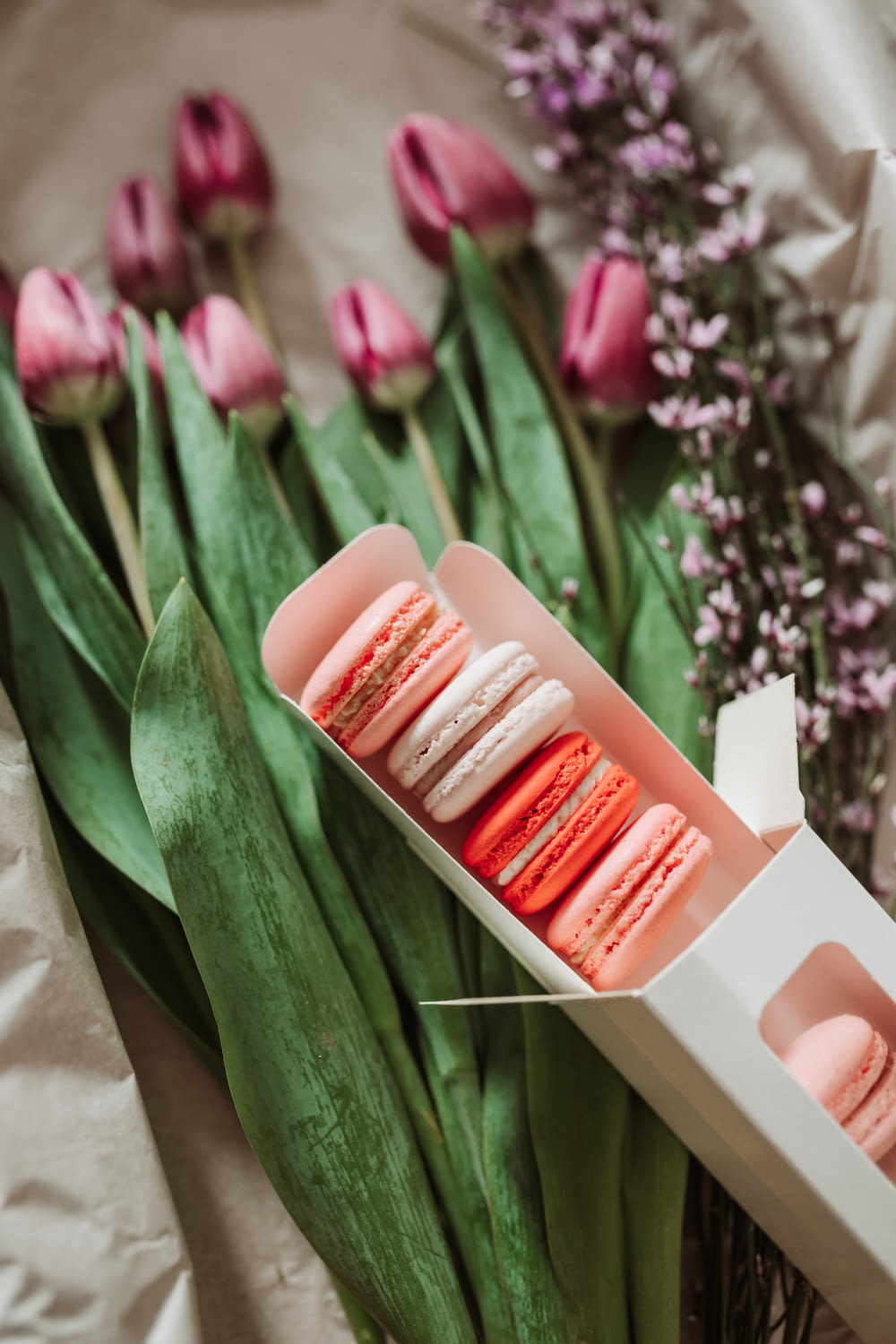 a box of macaroons sitting next to a bunch of flowers