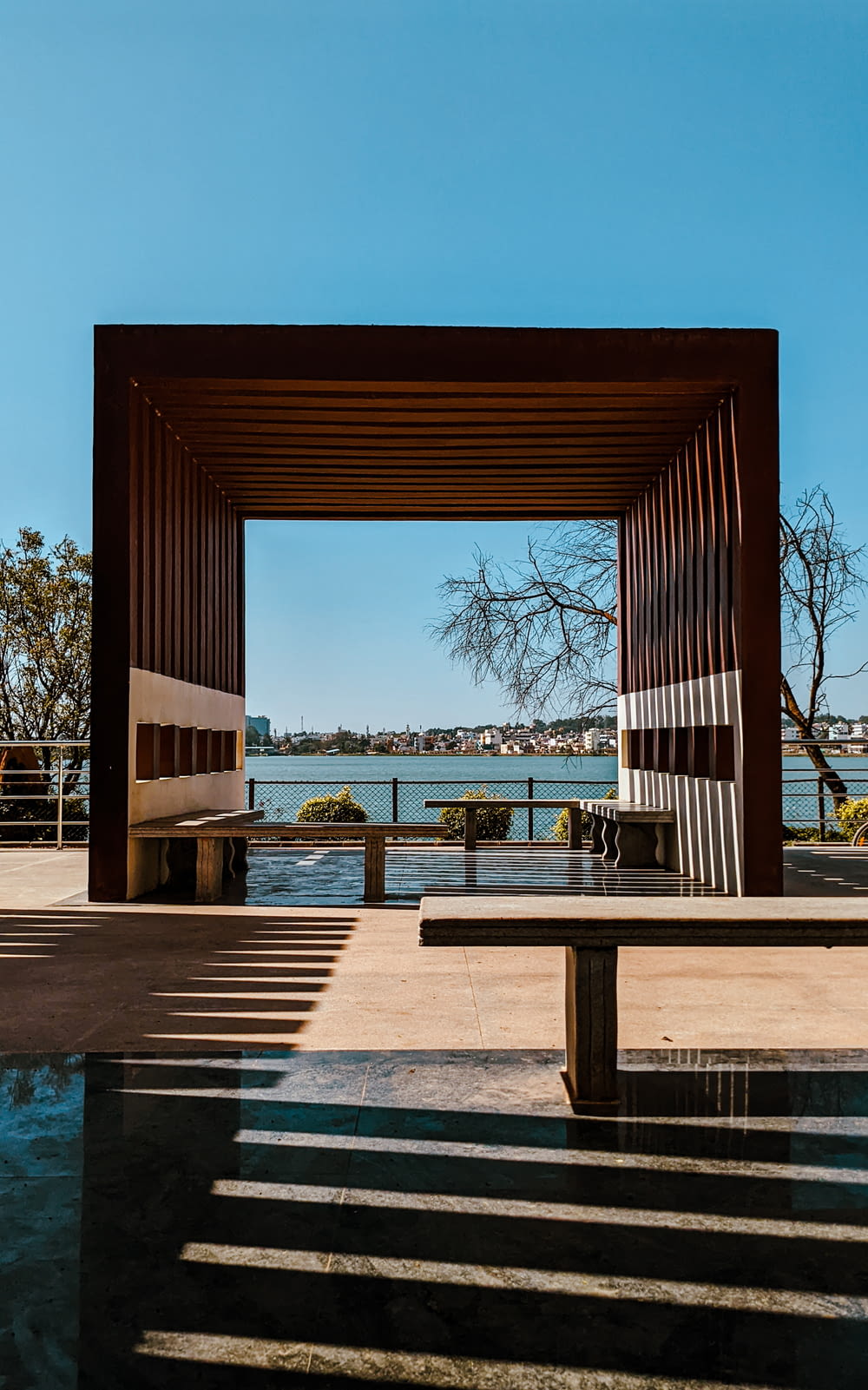 a bench sitting under a wooden structure next to a body of water