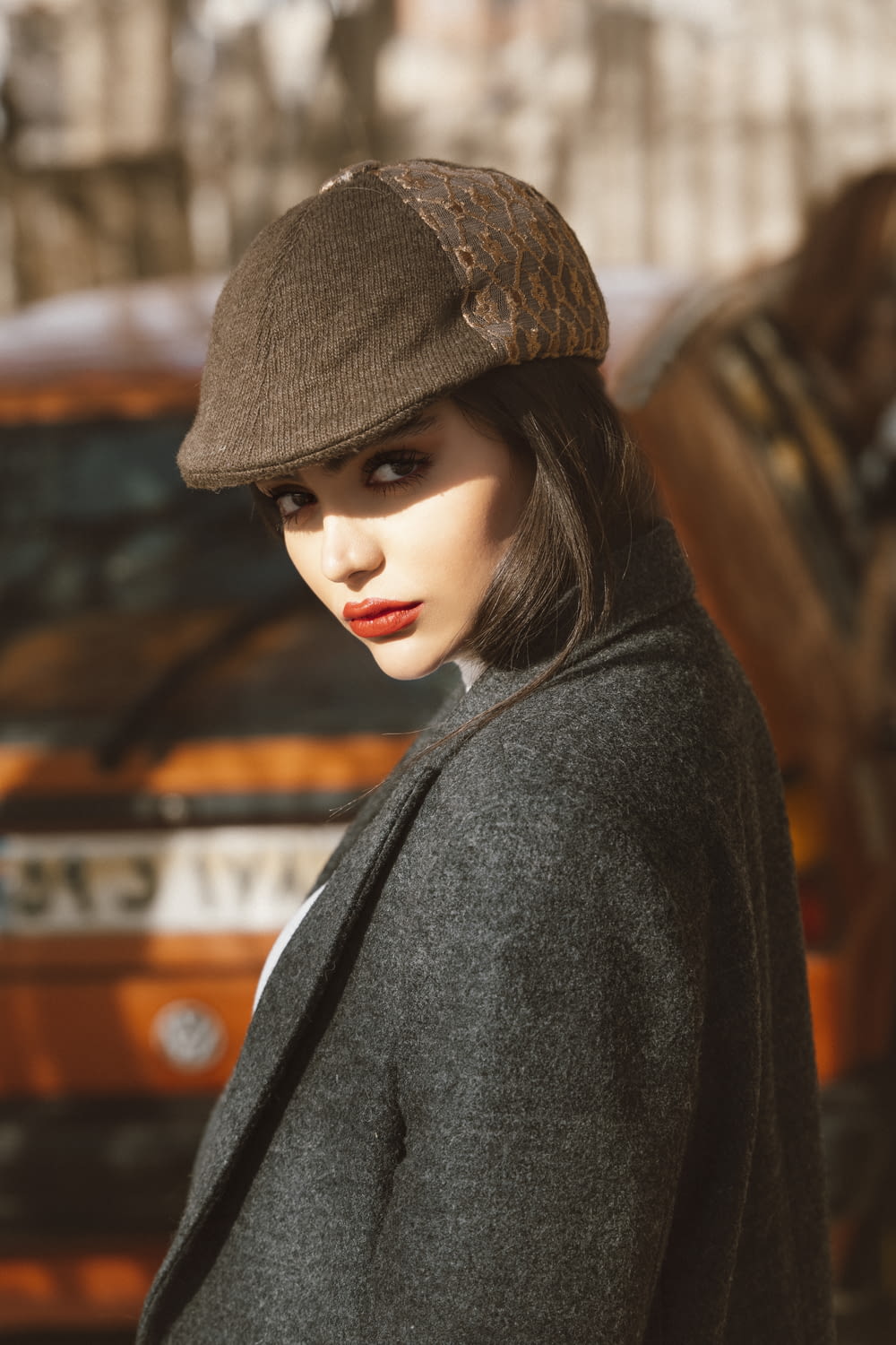 a woman in a hat and coat standing in front of a car