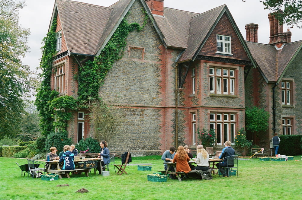 a group of people sitting at picnic tables in front of a large brick building