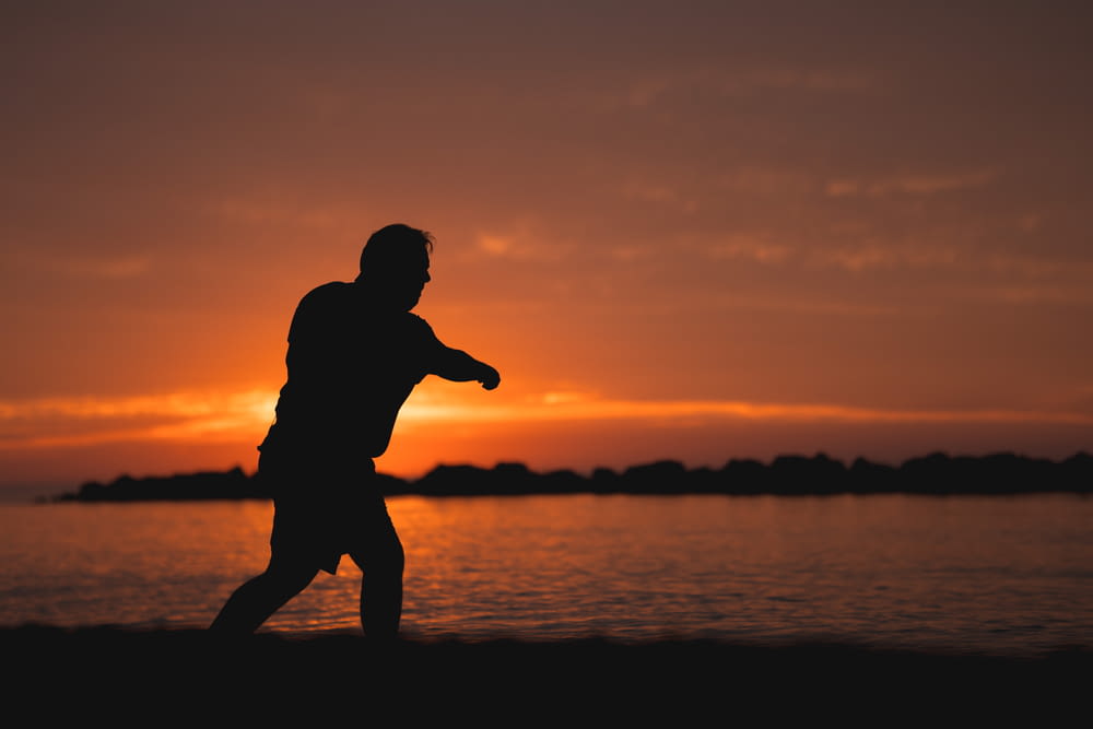 a silhouette of a man throwing a frisbee at sunset