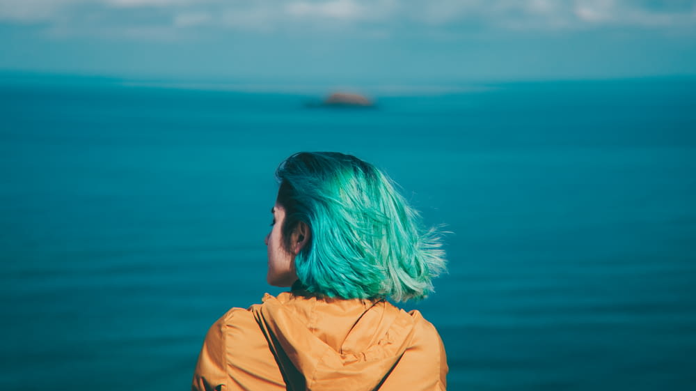 a woman with green hair looking out at the ocean
