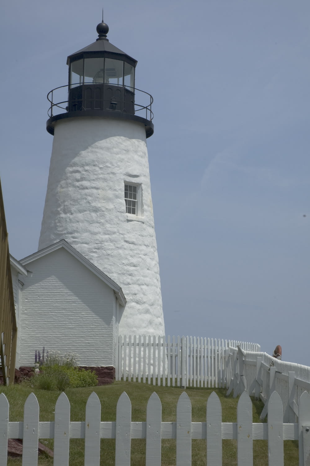 a white lighthouse with a black top and a white picket fence