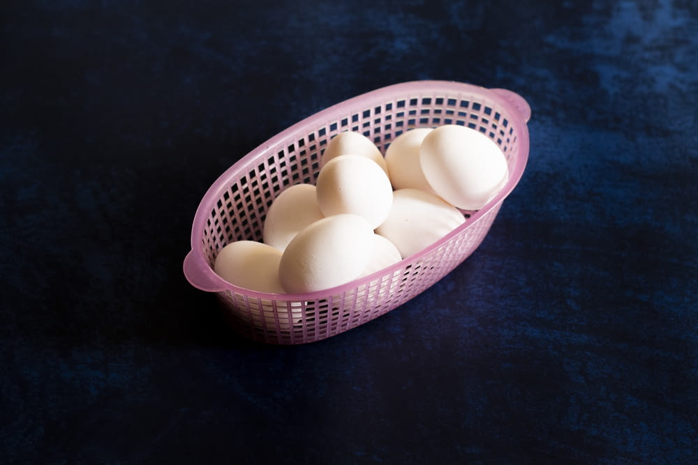 a pink basket filled with white eggs on top of a table