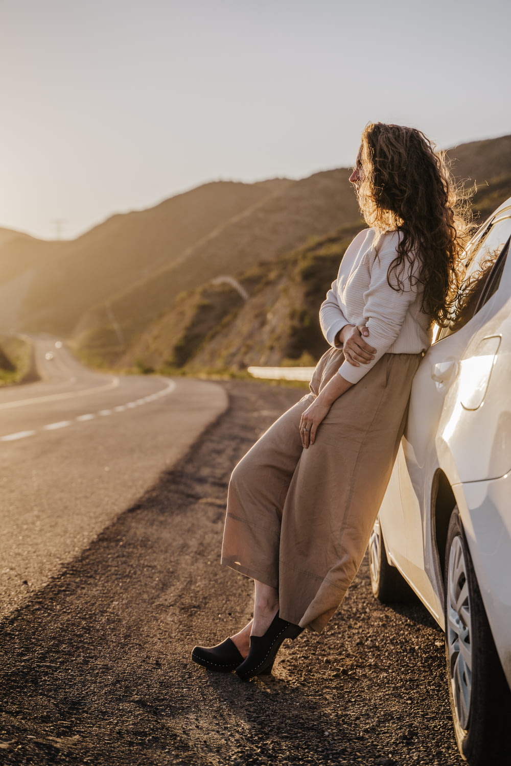 a woman leaning against a car on the side of the road