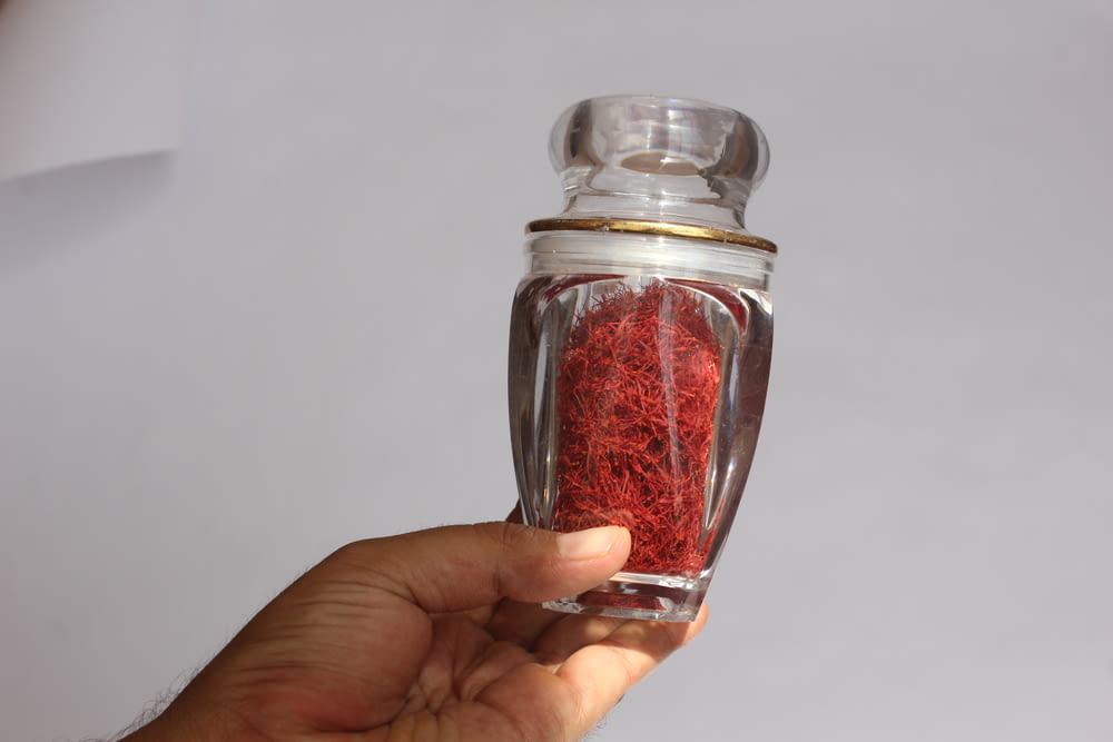a hand holding a jar filled with red sand