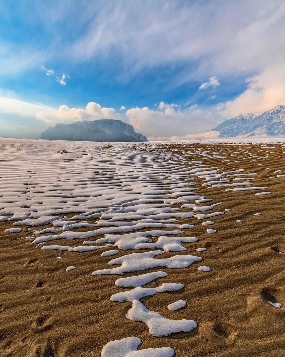 a sandy beach covered in snow under a blue sky
