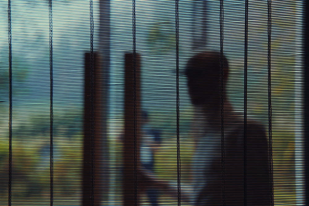 a person standing behind a window covered in blinds
