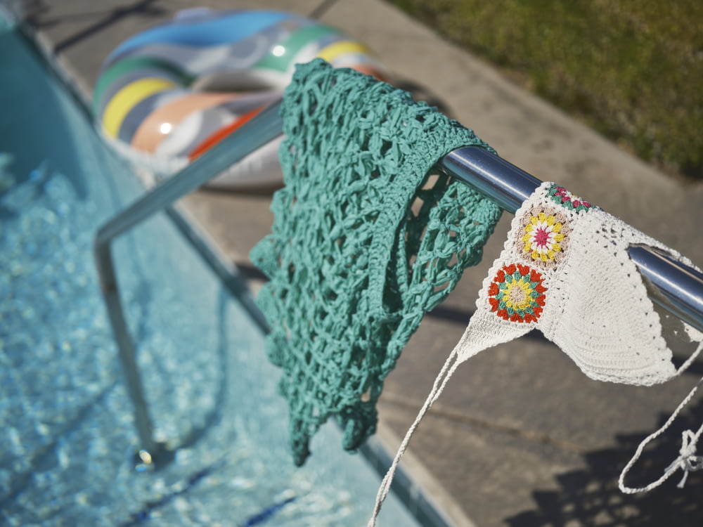 a green crocheted towel hanging on a rail next to a swimming pool
