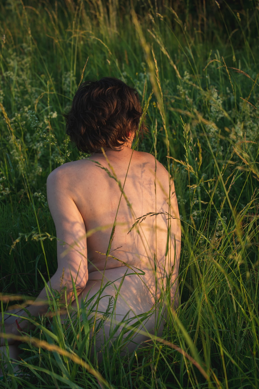 a naked man sitting in a field of tall grass
