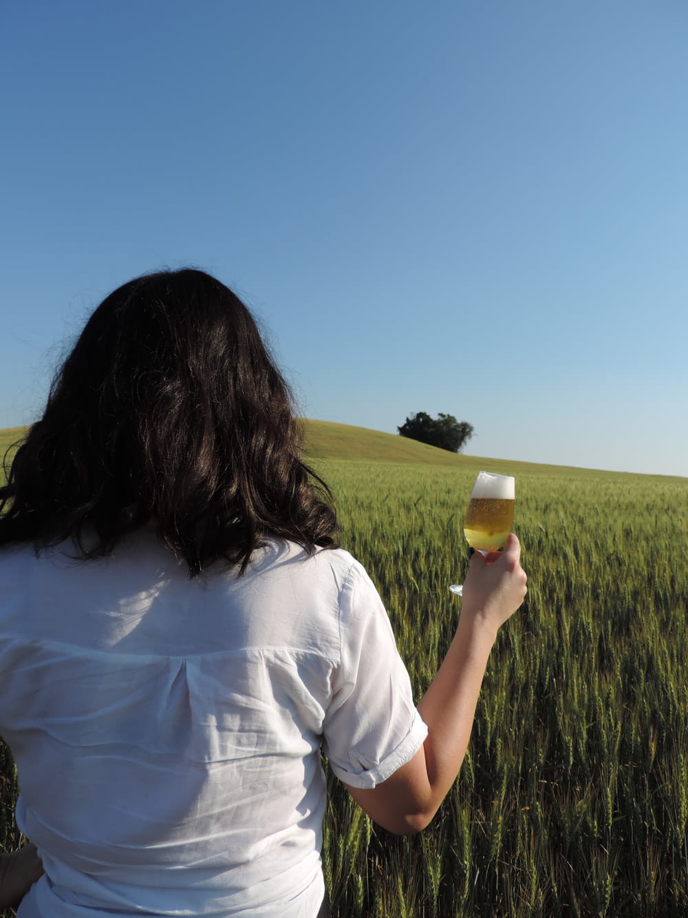 a woman standing in a field holding a glass of wine