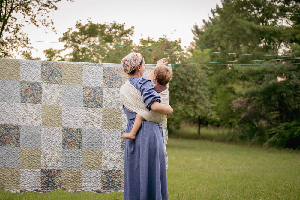 a woman holding a baby next to a quilt