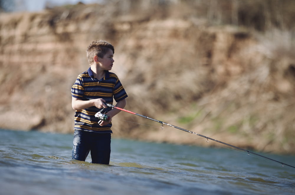 a young boy standing in the water holding a fishing rod