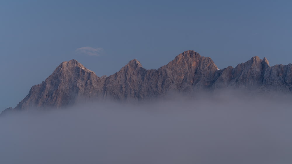 a very tall mountain covered in fog under a blue sky