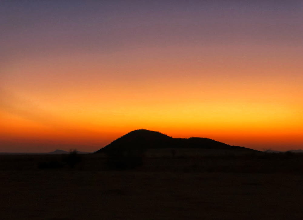 the sun is setting over a hill in the desert