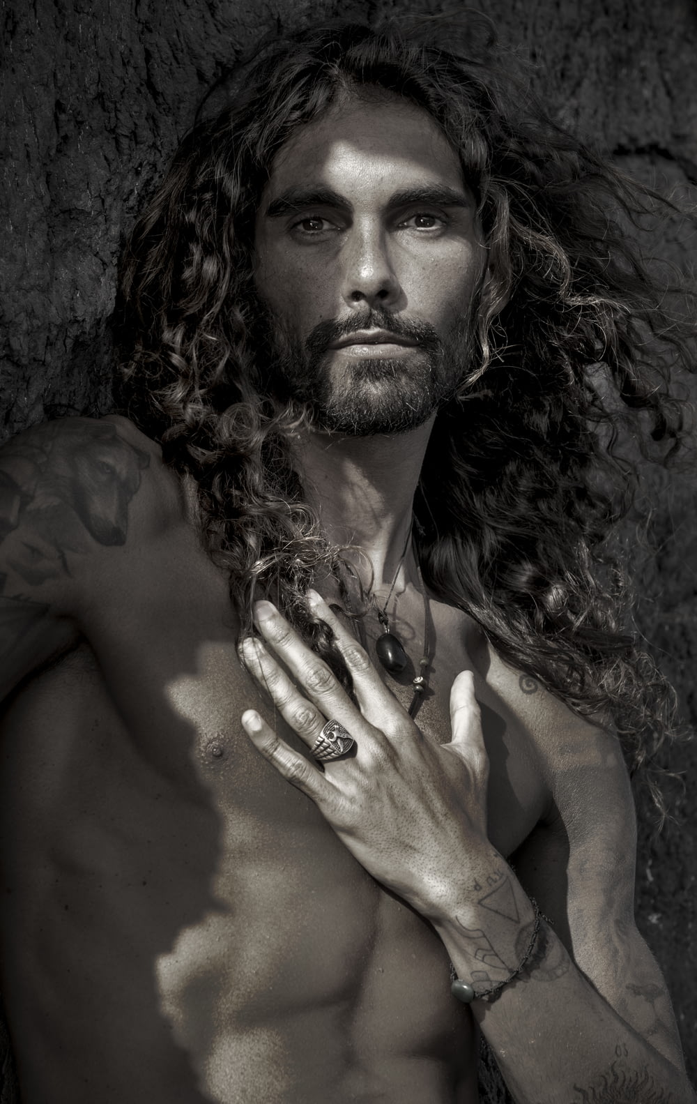 a shirtless man with long hair holding his hands together