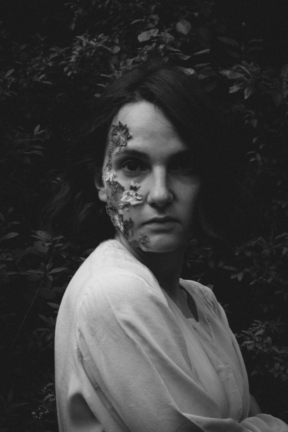a black and white photo of a woman with flowers on her face