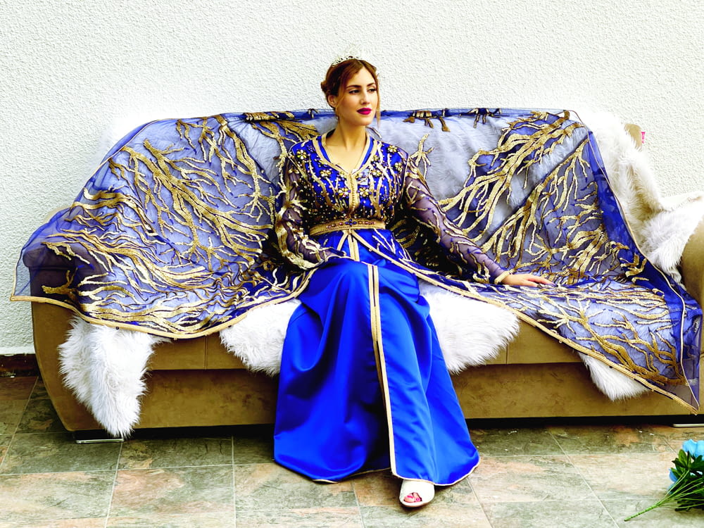 a woman sitting on a couch covered in a blue and gold blanket