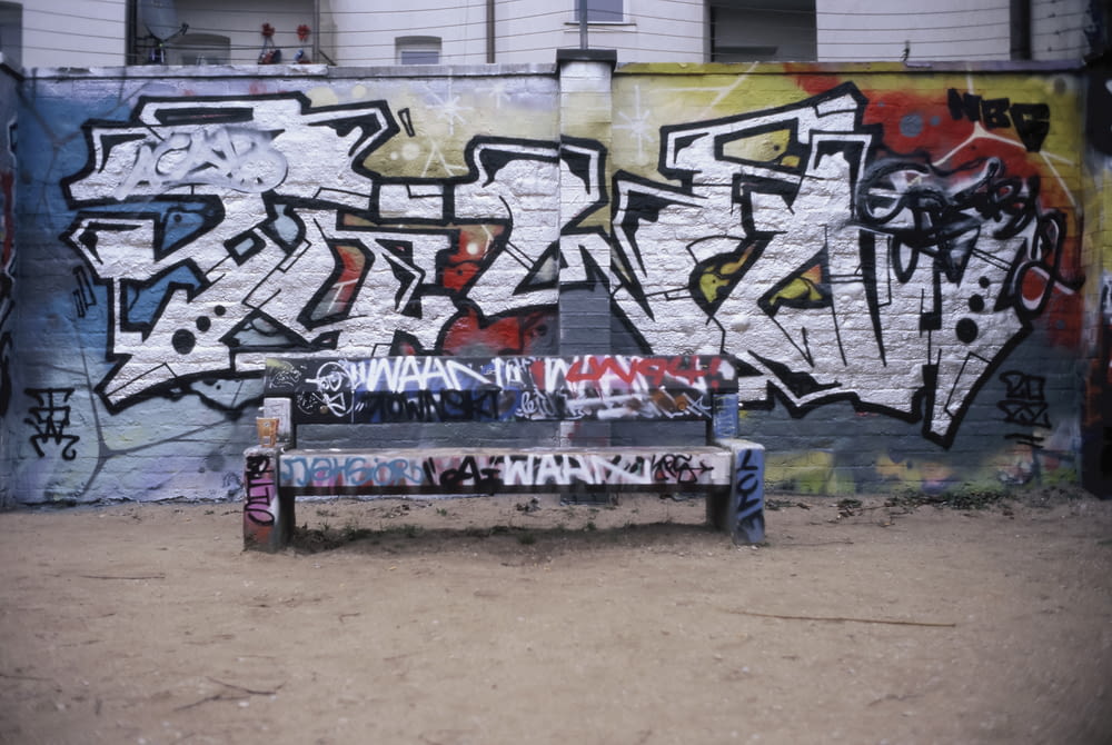 a bench in front of a graffiti covered wall