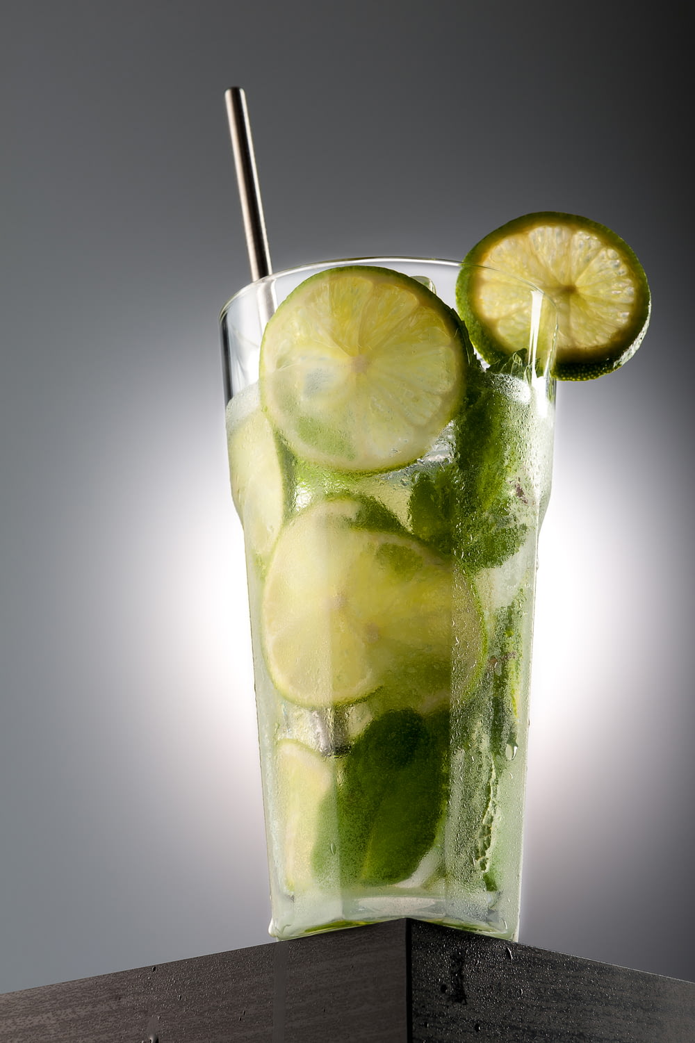 a glass of water with limes and a straw