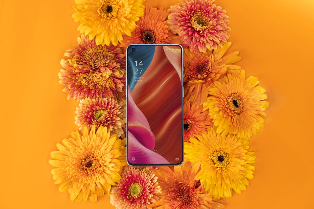 a cell phone surrounded by flowers on an orange background