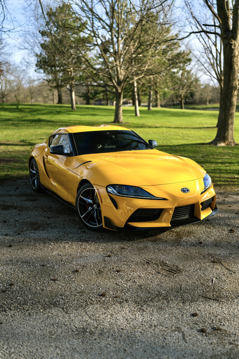a yellow sports car parked on a road with trees and grass