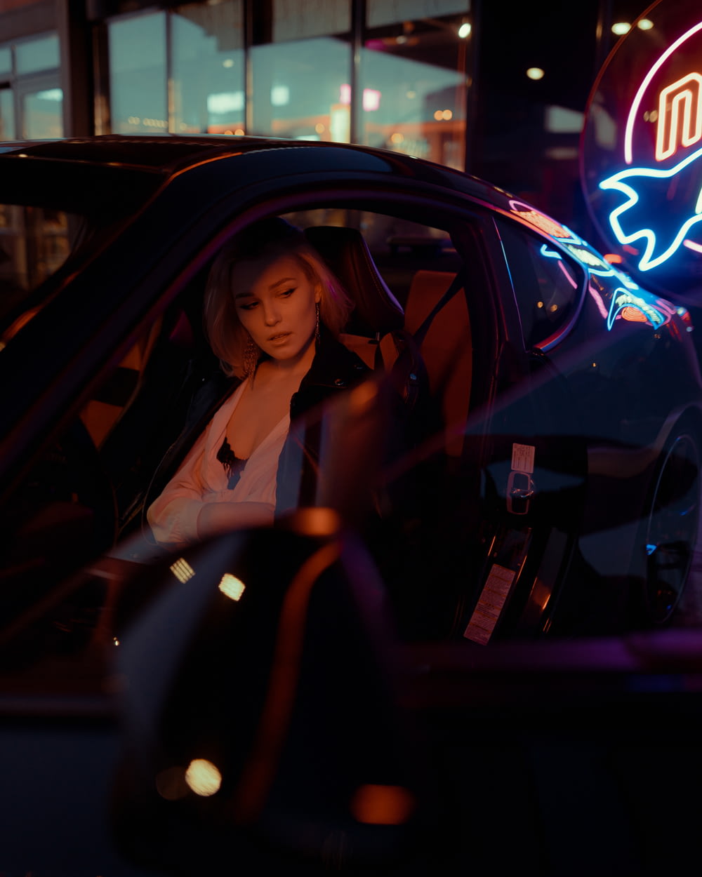 Una mujer sentada en un coche frente a un letrero de neón
