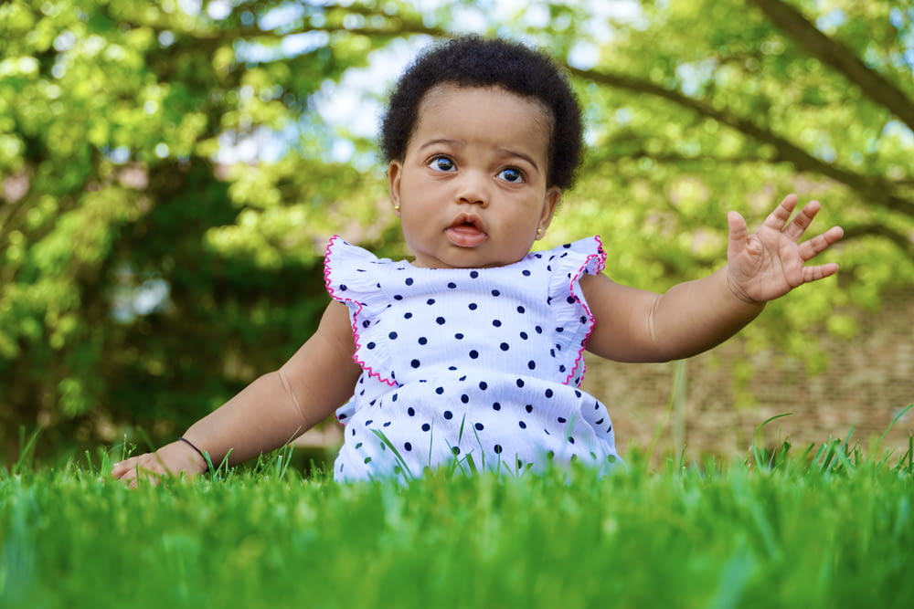 草の中に手を伸ばして座っている女の赤ちゃん