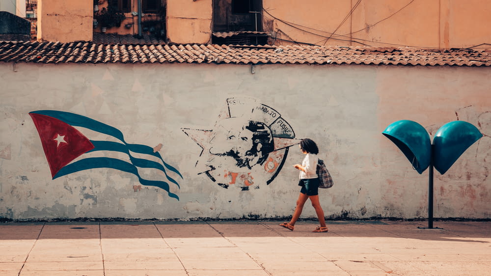 a woman walking past a wall with a flag painted on it